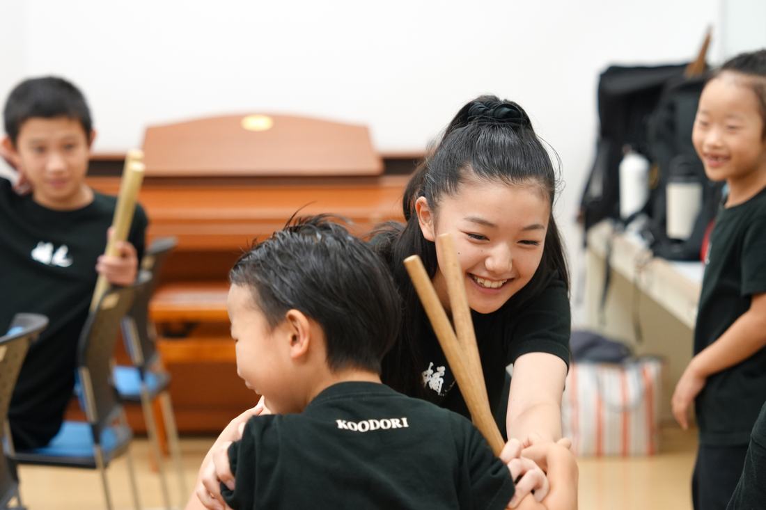 舞台裏でバチの持ち方を教わる子ども